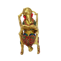 Craftearth's Handcrafted Decorative Brass Ganesha with Stone Work sitting on chair while reading | Study table decoration | study tablewear | decoration BR-320-A