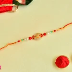 Golden Emblem Rakhi – RK-46 | Oval Centerpiece with Red Accents & Multicolor Bead Detailing