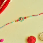 Traditional Floral Rakhi – RK-53 | Red-Blue Thread with Mirror Work & Gold Beads