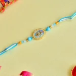 Aqua Bloom Rakhi – RK-61 | Oval Centerpiece with Crystal Detailing & Sky Blue Thread