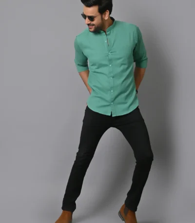 Men's casual fashion model in sunglasses wearing green shirt and black jeans standing against gray background, trendy and stylish menswear photography, CRAFTEARTH.